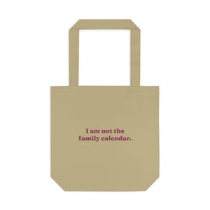 May include: A tan tote bag with two shoulder straps and the text "I am not the family calendar." printed in dark red lettering on the front. The bag features a rectangular body and a flat bottom, constructed from a solid-colored fabric material.