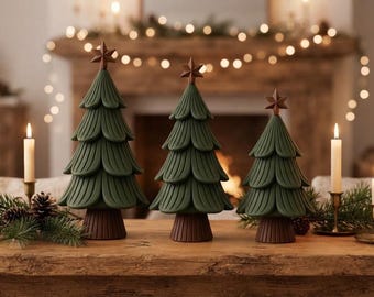 May include: Three decorative Christmas tree figurines in varying heights, each featuring a dark green, layered, scalloped foliage design, a brown ribbed trunk, and a small brown star topper. The trees are arranged in a row on a wooden surface.