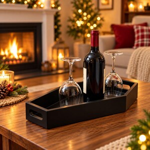 May include: A black coffin-shaped serving tray with cutout handles, holding a dark glass wine bottle with a red foil seal and two clear stemmed wine glasses positioned upright on the tray surface.