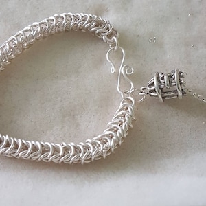 May include: A silver chain bracelet with a silver clasp and a silver charm in the shape of a cage.