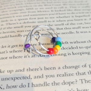 May include: A silver wire ring with a rainbow of coloured beads. The ring is wrapped in a spiral shape.