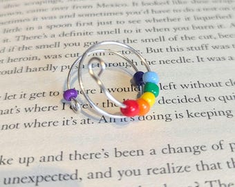 May include: A silver wire ring with a rainbow of colored beads. The ring is wrapped in a spiral shape.