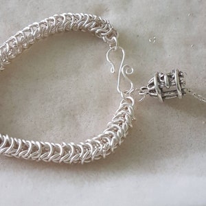 May include: A silver chain bracelet with a silver clasp and a decorative silver charm. The chain is made of small, interlocking links.