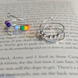 May include: Two silver hoop earrings with a rainbow of colored beads on one and a cluster of silver beads on the other.