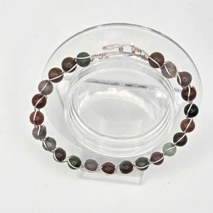 May include: A silver wire wrapped bracelet with multi-coloured agate beads. The beads are a mix of brown, red, green, and grey.