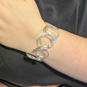 Könnte beinhalten: Silberarmband mit mehreren ineinander verschlungenen Kreisen und kleinen silbernen Perlen.