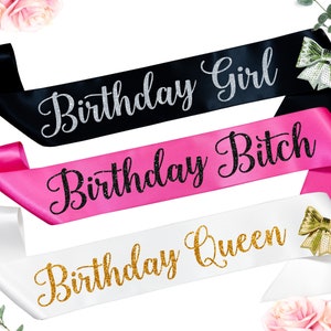 May include: Three satin sashes with glitter text. The sashes are black, pink, and white. The text on the sashes reads "Birthday Girl", "Birthday Bitch", and "Birthday Queen".