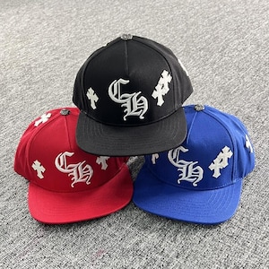 May include: Three baseball caps in black, red, and blue, each featuring a white embroidered CH monogram on the front panel and white cross emblems on the sides. Each cap has a flat brim and a metallic button detail at the crown.