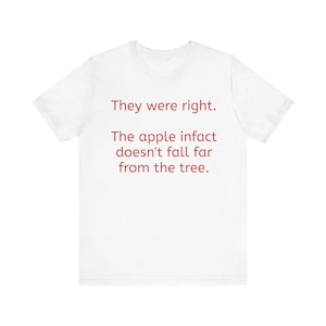 Puede incluir: Una camiseta blanca de manga corta con texto rojo impreso en la parte delantera que dice: They were right. The apple infact doesn't fall far from the tree. La prenda tiene cuello redondo y un corte estándar con la parte trasera blanca lisa.