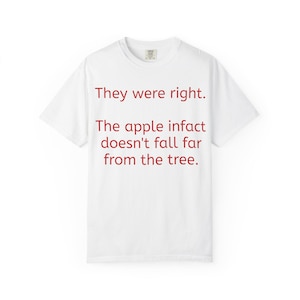Puede incluir: Una camiseta blanca de manga corta con texto rojo impreso en la parte delantera que dice: They were right. The apple infact doesn't fall far from the tree. La prenda tiene un cuello redondo y un corte estándar con una etiqueta de marca visible.