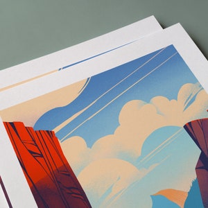 May include: A rectangular art print featuring a stylized landscape illustration with vibrant red rock formations on the left and dark purple cliffs on the right, set against a bright blue sky filled with soft, rounded cream-colored clouds.
