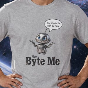 May include: A heather gray t-shirt featuring a small robot graphic with a speech bubble that says, "You should be rich by now." Below the robot, the text reads, "Me: Byte Me" in a distressed, dark gray, bold, sans-serif font.