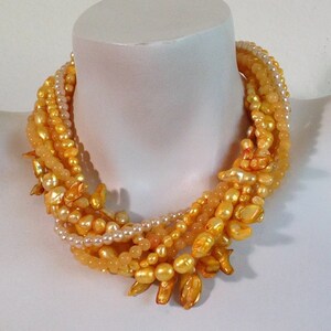 May include: A multi-strand necklace made of small, round, cream-colored pearls and larger, irregular, golden-yellow pearls. The necklace is layered and has a cascading effect.