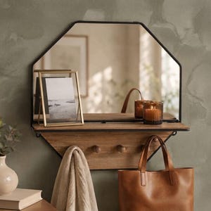 May include: An octagonal wall mirror with a black metal frame and an integrated wooden shelf. The shelf features three wooden pegs for hanging items. A gold-toned picture frame and a ribbed glass candle holder sit on the wooden surface.