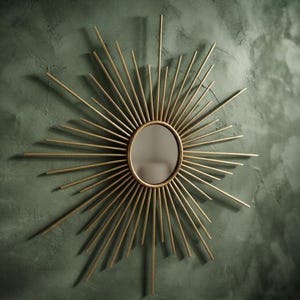 May include: A circular wall mirror featuring a gold-toned frame with numerous thin, radiating metal spokes that extend outward in a sunburst pattern. The central mirror is round and smooth, surrounded by a metallic structure with varying lengths.