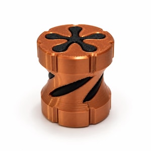 Könnte beinhalten: Ein zylindrisches Objekt mit metallisch kupferfarbenem Finish und schwarzem Kern. Die Oberseite weist einen sternförmigen Ausschnitt mit fünf Zacken auf, während die Seiten diagonale, spiralförmige schwarze Rillen zeigen.