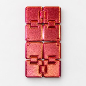 K&ouml;nnte beinhalten: Ein Fidget-Spielzeug bestehend aus acht miteinander verbundenen quadratischen Segmenten mit einer metallisch schimmernden Oberfl&auml;che, die zwischen leuchtendem Rot, Orange und Magenta wechselt. Jeder quadratische Teil hat eine texturierte Kreuzschraffur.