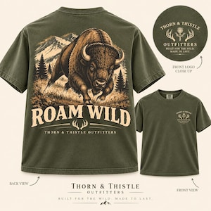 May include: An olive green t-shirt featuring a large graphic on the back of a bison in a mountain landscape with the text ROAM WILD and THORN & THISTLE OUTFITTERS. The front chest displays a small circular logo with the same brand name.
