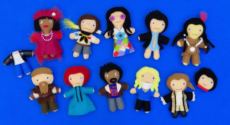 May include: A collection of handmade felt dolls, each depicting a different character. The dolls vary in color and design, with some wearing outfits and accessories. The dolls are arranged on a blue surface.