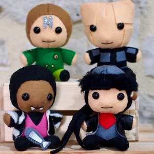 Pode incluir: Quatro peluches, cada uma com um design e cor diferentes. O primeiro brinquedo é marrom com uma roupa verde e uma letra H prateada na testa. O segundo brinquedo é bege com uma roupa cinza e preta. O terceiro brinquedo é marrom com uma jaqueta listrada preta e branca e uma camisa rosa. O quarto brinquedo é cinza com cabelo preto e uma jaqueta preta com um coração vermelho.