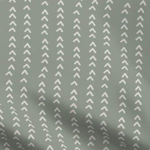 May include: A textile featuring a repeating pattern of white chevron arrows arranged in vertical columns on a muted green background. The arrows point upwards, creating a textured, directional design.