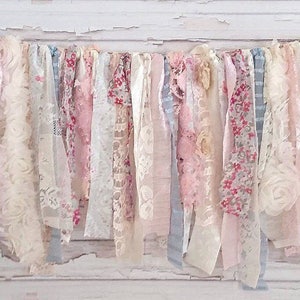 May include: A decorative banner made of various fabrics, including lace, floral print, and burlap. The banner features a mix of pink, white, and blue colors and is adorned with burlap flowers.