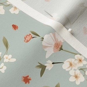 May include: Close-up of a light blue fabric with a white floral pattern. The fabric has a white trim along the edge and a pin is holding the fabric together.