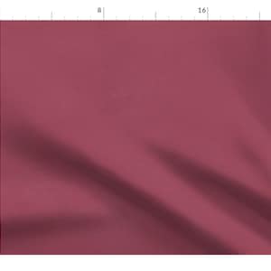 May include: A close-up of a smooth, deep red fabric with a slight sheen. The fabric is draped and folded, creating soft curves and folds.