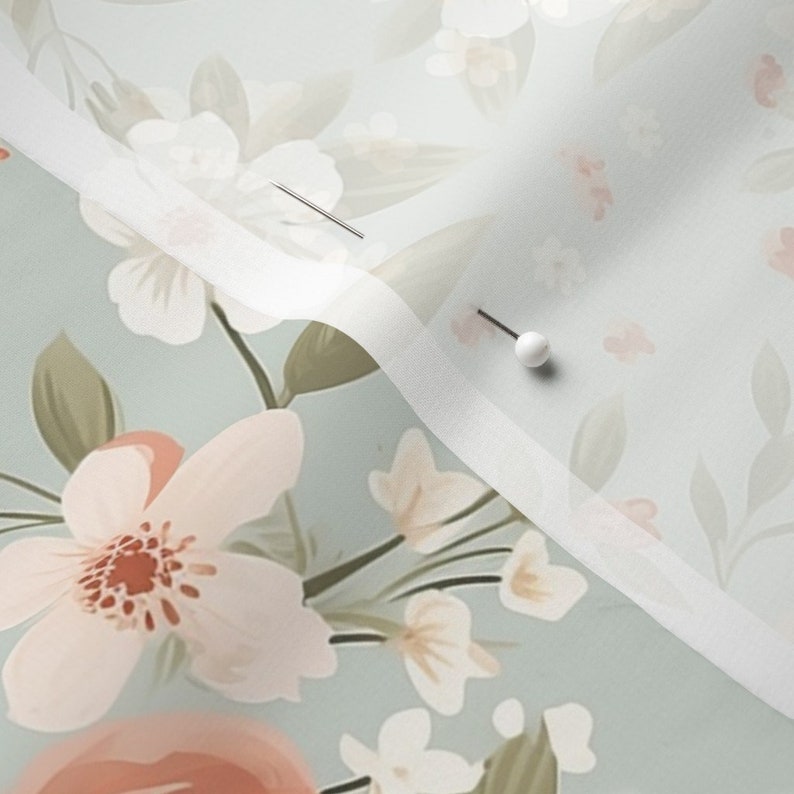 May include: A light blue fabric with a white floral pattern. The fabric is folded in half and pinned together with a white pin.