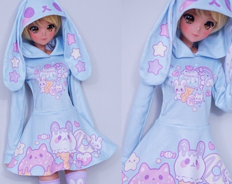 May include: A light blue hooded dress with bunny ears, featuring a print of cartoon animals and sweets. The dress has a flared skirt and long sleeves.