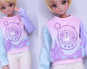 May include: A pink and blue sweatshirt with a graphic of a purple and white digital pet with a sleeping bunny inside. The sweatshirt has a light blue and pink ombre effect.