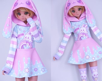 May include: A pink and blue doll outfit with a bunny hood, long sleeves, and a skirt. The outfit has a rainbow, stars, and a bunny graphic. The text "Kawaii" is printed on the outfit.