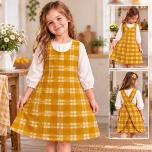May include: A mustard yellow and white plaid pinafore dress worn over a white long-sleeved blouse with ruffled cuffs. The dress features a scoop neckline and a flared skirt. The back of the dress has wide, overlapping straps that cross over.