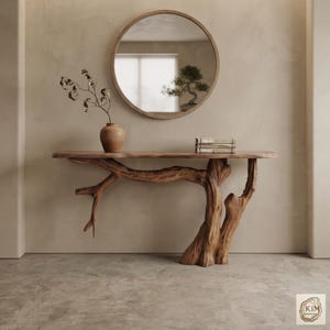May include: A console table with a smooth, flat wooden top supported by a base shaped like a natural tree trunk and branches. A round mirror hangs above the table, which holds a small ceramic vase with a branch and a stack of three books.
