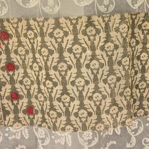 May include: A sample of fabric with a floral pattern in shades of gray and cream, held together with three red buttons. The fabric is set against a backdrop of sheer white curtains with a delicate floral design.