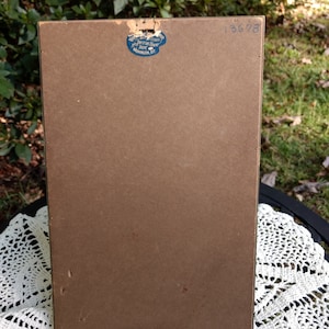 May include: The back of a brown picture frame with a blue sticker that says "Art Interiors Picture Frame Co. Washington D.C." and the number "13678" written in black ink.