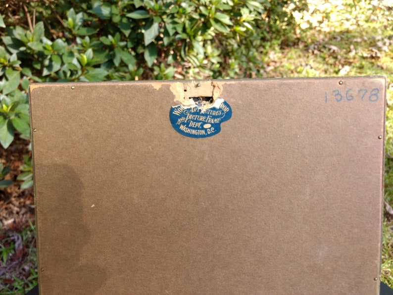 May include: The back of a brown picture frame with a blue sticker that reads "Wood Art Pictures Picture Frame Dept. Washington, D.C." and the number "13678" written in blue ink.