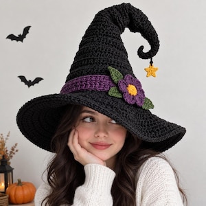 Puede incluir: Un sombrero de bruja de ganchillo negro con una banda morada, una flor morada y amarilla con hojas verdes y un pequeño dije de estrella amarilla que cuelga de la punta curvada. El sombrero tiene un ala ancha y una copa alta y puntiaguda.