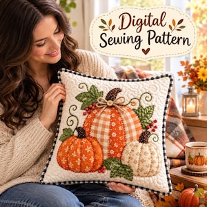 May include: A square quilted throw pillow featuring an appliqué design of three pumpkins in orange, white, and plaid fabrics, accented with green leaves, red berries, and a small wooden button, finished with a black and white checkered border.