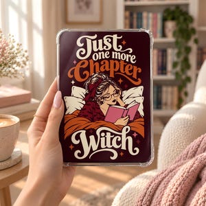 Op de afbeelding: Een doorzichtige tablethoes met een grafische illustratie van een persoon die in bed een boek leest. De tekst Just one more Chapter Witch staat in crème- en oranjegekleurde letters op een donkere achtergrond met kleine sterren.