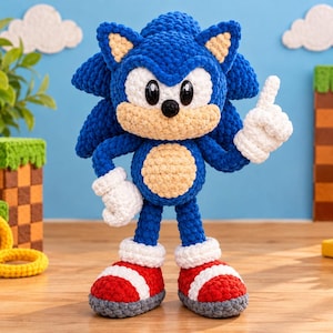Könnte beinhalten: Ein handgefertigtes Häkel-Plüschtier der Figur Sonic the Hedgehog. Die Figur besteht aus leuchtend blauem Garn, hat eine beigefarbene Schnauze und einen Bauch, weiße Handschuhe sowie rot-weiße Turnschuhe. Sie besitzt große schwarze Kunststoffaugen.