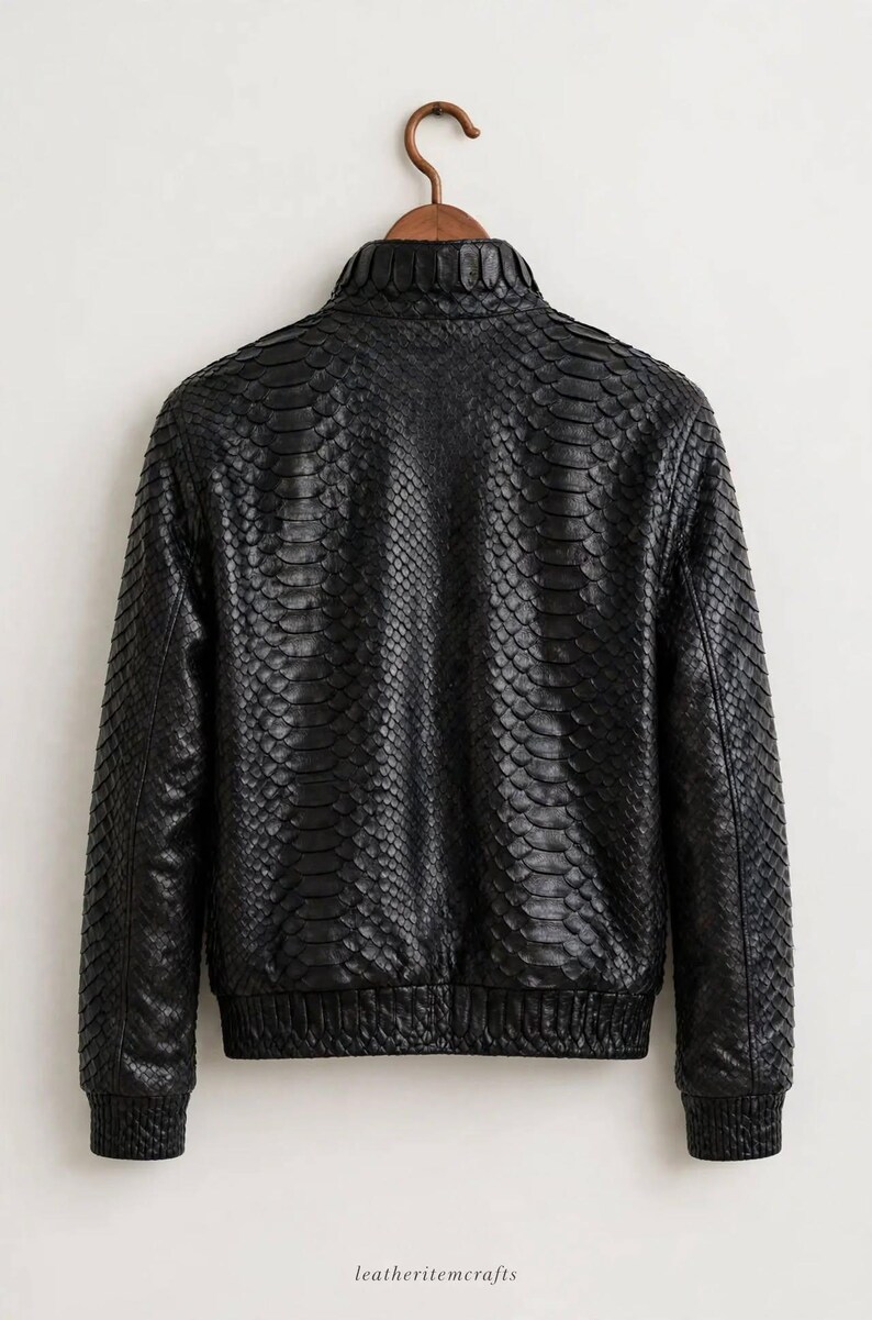 May include: A black jacket featuring a textured snakeskin pattern throughout the entire garment. The jacket includes a high collar, long sleeves with ribbed cuffs, and a ribbed hemline. The text leatheritemcrafts is printed at the bottom.