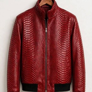 May include: A deep red jacket featuring a textured snakeskin-like pattern, a central silver zipper, a high collar, and black ribbed cuffs and hem. The text "leatheritemcrafts" is printed in small black letters at the bottom center.