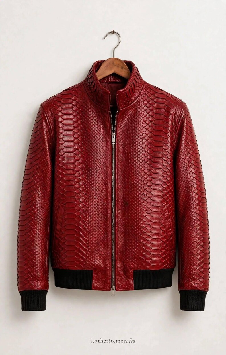 May include: A deep red jacket featuring a textured snakeskin-like pattern, a central silver zipper, a high collar, and black ribbed cuffs and hem. The text "leatheritemcrafts" is printed in small black letters at the bottom center.