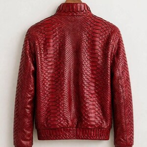 May include: A red jacket featuring a textured snakeskin pattern throughout the exterior. The garment includes a high collar, long sleeves with ribbed cuffs, and a ribbed hemline. The text leatheritemcrafts is visible at the bottom.
