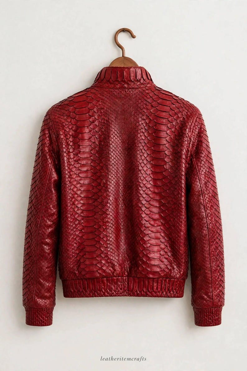 May include: A red jacket featuring a textured snakeskin pattern throughout the exterior. The garment includes a high collar, long sleeves with ribbed cuffs, and a ribbed hemline. The text leatheritemcrafts is visible at the bottom.