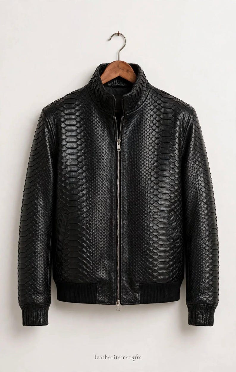 May include: A black jacket featuring a textured snakeskin pattern throughout the exterior. The garment includes a central silver-toned zipper, a high collar, and black ribbed cuffs and hem. The text leatheritemcrafts is visible at the bottom.