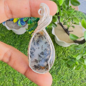 May include: A teardrop-shaped dendritic agate pendant encased in a silver-coloured wire-wrapped setting. The stone features a translucent white base with dark, fern-like inclusions spreading across the surface, topped with a coiled wire bail.