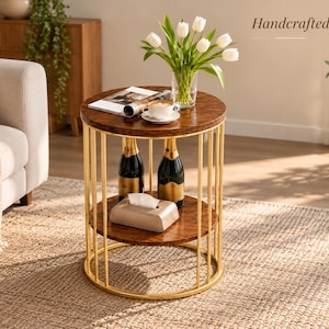 Puede incluir: Una mesa auxiliar redonda con dos estantes de madera oscura y un marco de metal dorado formado por barras verticales. La mesa sostiene un jarrón de cristal con tulipanes blancos, una revista, una taza, dos botellas oscuras y una caja de pañuelos.