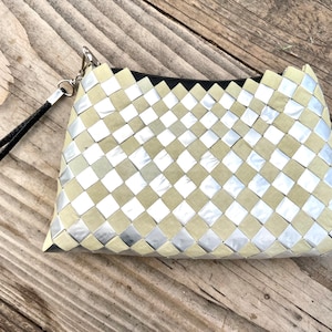 May include: A small, silver and beige woven clutch bag with a black strap. The bag is made of woven squares of fabric.